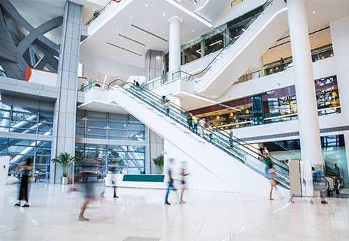 image of a mall atrium with escalators and consumers rushing about